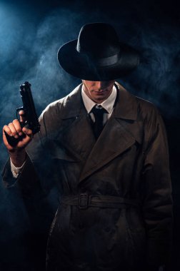 Silhouette of a male detective in a coat and hat with a gun in his hands. A dramatic noir portrait in the style of books and detective films of the 1950s