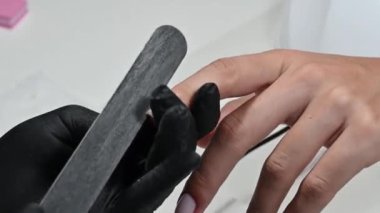 A manicure master does a manicure to a girl in the salon. Nails are filed with a file. Close-up.