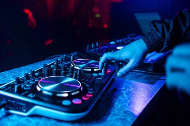 DJ console mixing music hands and with blurred people dancing night club party