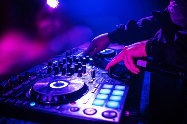DJ console mixing music hands and with blurred people dancing night club party