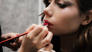 Make-up artist makes lip makeup art for a young girl in a beauty salon. Red lipstick. Unusual makeup
