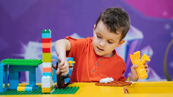 Educational toys. A picture of a boys child playing with colorful plastic bricks at a table. The kid has fun and builds from bright constructor cubes. Early learning