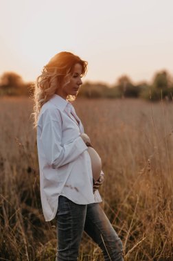 Doğada batan güneşin altında bekleyen hamile bir annenin silueti. Hamilelikte sakinlik kavramı. Üçüncü üç aylık dönem