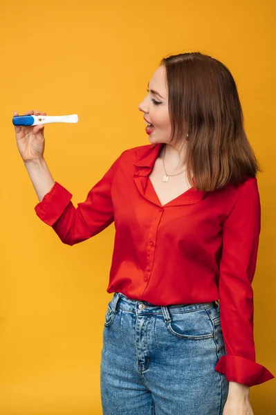 Studio shot of an emotional young woman with a positive pregnancy test in her hands. An expression of surprise and joy on his face. The concept of pregnancy, motherhood