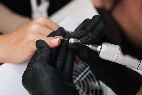 修指甲师在电机上用刀具加工指甲表面的修指甲师的特写 去除毛刺 专业美容院的概念 — 图库照片