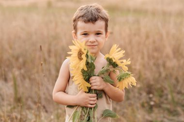 Güneşli bir yaz akşamında elinde kocaman bir buket çiçek tutan, ayçiçeği tarlasında gülen sevimli bir çocuk. Altın saat