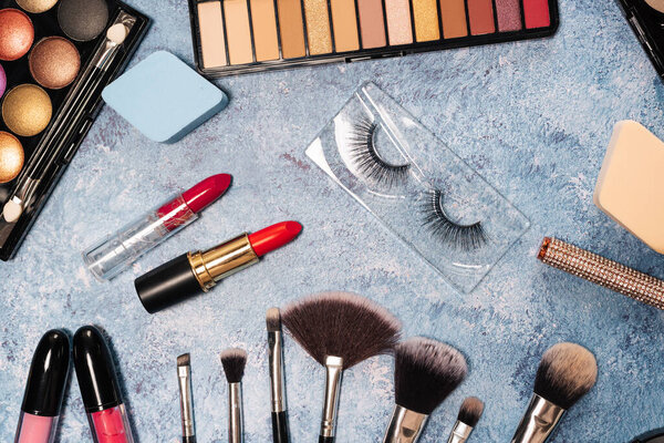 set decorative cosmetics, makeup brushes false eyelashes blue background. view from top