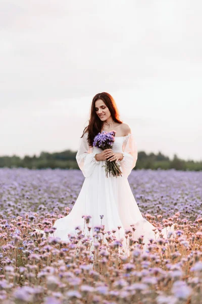 彼女の手に花束とロマンチックな雰囲気の中でプロバンスの開花フィールドで白いドレスの美しい女の子 — ストック写真