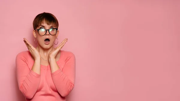 stock image Portrait of a surprised attractive Caucasian girl isolated on a pink background, holding her head with her hands in amazement and with her mouth open. Copying space. Advertisement