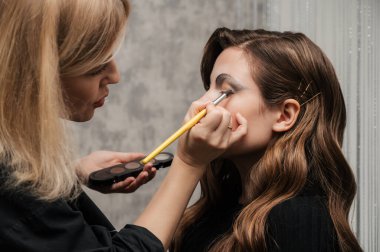 Makyaj sanatçısı güzellik salonunda genç bir kız için göz makyajı yapıyor. Cadılar Bayramı kutlaması. Alışılmadık makyaj