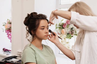 Güzellik salonunda çekim yapmak. Makyaj ustası temeli fırçayla gölgeliyor.