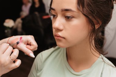 Güzellik salonunda çekim yapmak. Makyaj ustası, modelin dudaklarındaki ruju fırçayla gölgeliyor..