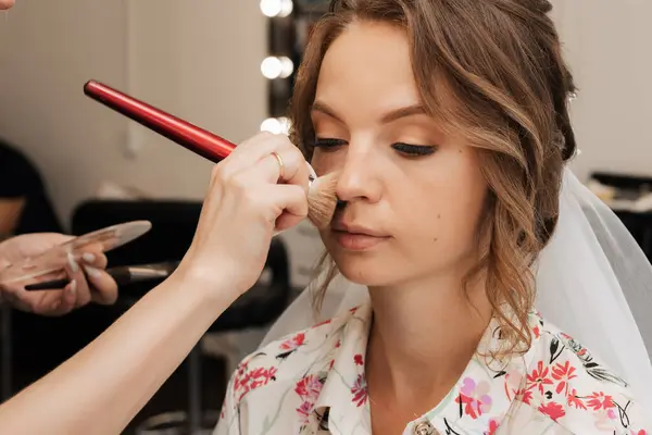 Shooting in a beauty salon. makeup artist applies makeup to a young beautiful girl bride