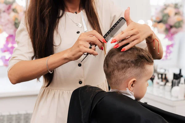 Shooting in a beauty salon. A hairdresser gives a haircut to a little boy with scissors