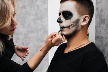 Bir makyaj sanatçısı güzellik salonunda genç bir adam için iblis makyajı yapar. Cadılar Bayramı Kutlaması Kavramı.