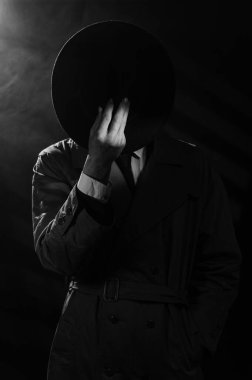 Yağmurluk giymiş bir adamın koyu bir silueti ve kara film tarzında bir şapka. 1950 'lerin dedektiflerinin dramatik siyah portresi. Fotoğrafta duman var..