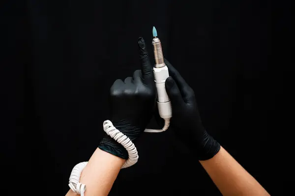 A machine for professional hardware manicure in a womans hand on a black background. Equipment for the nail service master. Cosmetic procedures