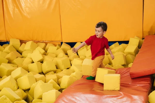 A boy is playing in a game entertainment nursery. He plays with soft large cubes. Active pastime in the amusement park. Trampolines and a dry pool