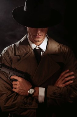 Silhouette of a male detective in a coat and hat with a gun in his hands. A book drama noir portrait in the style of detectives of the 1950s