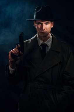 Silhouette of a male detective in a coat and hat with a gun in his hands. A book drama noir portrait in the style of detectives of the 1950s