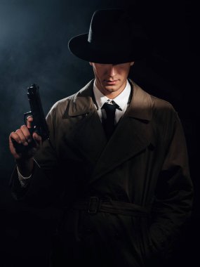 Silhouette of a male detective in a coat and hat with a gun in his hands. A dramatic noir portrait in the style of books and detective films of the 1950s