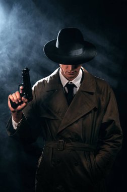 Silhouette of a male detective in a coat and hat with a gun in his hands. A dramatic noir portrait in the style of books and detective films of the 1950s