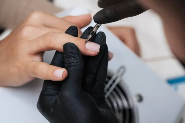 A manicure master gives a manicure to a girl in the salon. Close-up. The manicure master cuts the cuticle and burrs with manicure scissors