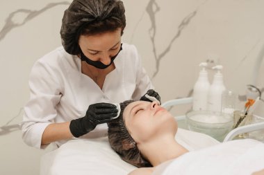 Kozmetik uzmanı, müşterinin derisini pamukla temizler.