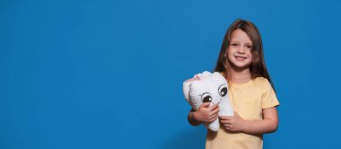 Sağlıklı dişleri olan gülümseyen bir kız mavi izole bir arka planda elinde bir diş oyuncağı tutuyor. Mesajın için bir yer. Ağız temizliği. Pediatrik dişçilik. Protezler. Diş fırçalama kuralları