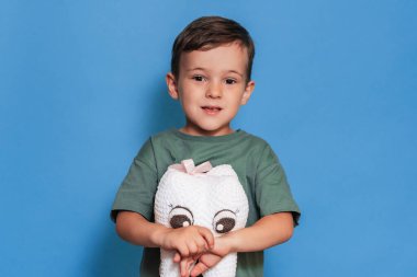 Sağlıklı dişleri olan gülümseyen bir çocuk mavi arka planda pelüş bir diş tutar. Ağız temizliği. Pediatrik dişçilik. Taşıyıcıların Önlenmesi