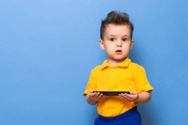 Küçük çocuk elinde bir cep telefonu tutuyor. Mavi arka planda stüdyo fotoğrafı. Metin için boşluk