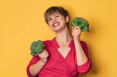 Sarı arka planda gülümseyen narin bir kadının elinde brokoli. sağlıklı yaşam tarzı