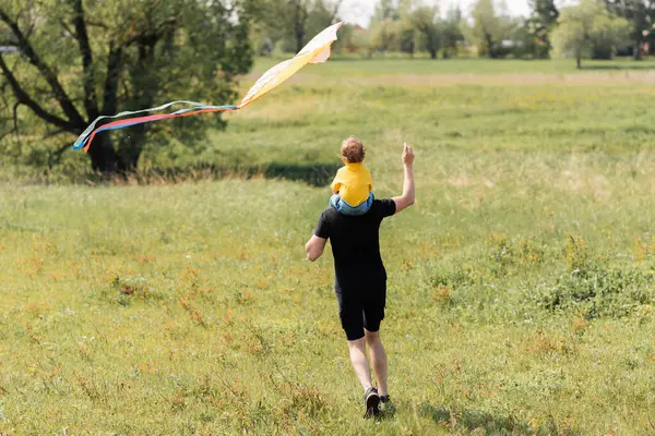 father and son run in the field with kite
