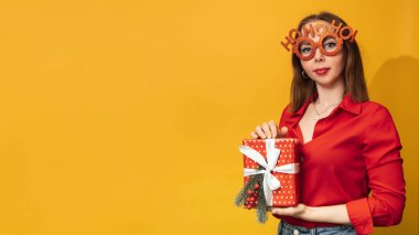 Sarı arka planda elinde Noel kutusuyla genç bir kadın. Noel 'i ve yeni yılı kutlama konsepti. Metnin için bir yer