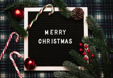 Eski bir mektup panosundaki plastik harflerle mutlu noeller. Her yerde karamel kamışlar, toplar, koniler ve köknar dalları var. Üst Manzara. Düz çizgi. Hazır Noel tebrik kartı.