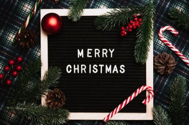 Eski bir mektup panosundaki plastik harflerle mutlu noeller. Arka planda karamel kamışlar, toplar, koniler ve köknar dalları var. Üst Manzara. Düz çizgi. Noel tebrik kartı.