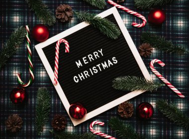 Eski bir mektup panosundaki plastik harflerle mutlu noeller. Arka planda karamel kamışlar, toplar, koniler ve köknar dalları var. Üst Manzara. Düz çizgi. Noel tebrik kartı.