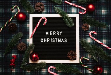 Eski bir mektup panosundaki plastik harflerle mutlu noeller. Her yerde karamel kamışlar, toplar, koniler ve köknar dalları var. Üst Manzara. Düz çizgi. Hazır Noel tebrik kartı.