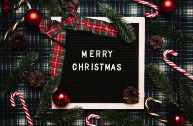 Eski bir mektup panosundaki plastik harflerle mutlu noeller. Arka planda karamel kamışlar, toplar, koniler ve köknar dalları var. Üst Manzara. Düz çizgi. Noel tebrik kartı.