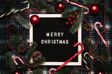 Eski bir mektup panosundaki plastik harflerle mutlu noeller. Her yerde karamel kamışlar, toplar, koniler ve köknar dalları var. Üst Manzara. Düz çizgi. Hazır Noel tebrik kartı.