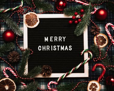 Bir mektup tahtasına plastik harflerle yazılmış mutlu noeller. Karamel kamışları, toplar, koniler, köknar dalları ve kurutulmuş portakallar var. Noel tebrik kartı..