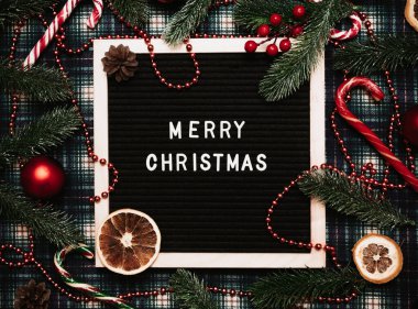 Bir mektup tahtasına plastik harflerle yazılmış mutlu noeller. Karamel kamışları, toplar, koniler, köknar dalları ve kurutulmuş portakallar var. Noel tebrik kartı..