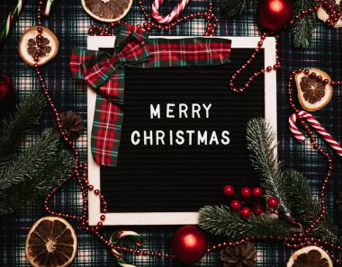 Bir mektup tahtasına plastik harflerle yazılmış mutlu noeller. Karamel kamışları, toplar, koniler, köknar dalları ve kurutulmuş portakallar var. Noel tebrik kartı..