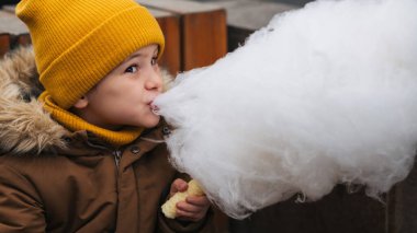 Küçük çocuk parkta çubukta pamuk şeker yiyor.