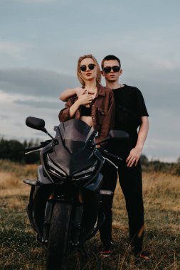Sarılan genç ve güzel bir çift kırsalda bir spor motosikletinin yanında duruyorlar..