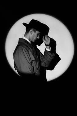 A dark silhouette of a male detective in a coat and hat in the noir style. A dramatic portrait in the style of detective films of the 1950s. A silhouette in a circle of light, like Agent 007