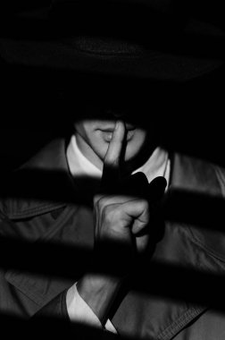 Paltolu ve şapkalı bir erkek dedektifin koyu renk silueti siyah tarzında gizli bir işaret gösteriyor. 1950 'lerin dedektif filmlerinin dramatik siyah portresi. Perdelerle ilgili dramatik bir ışık.