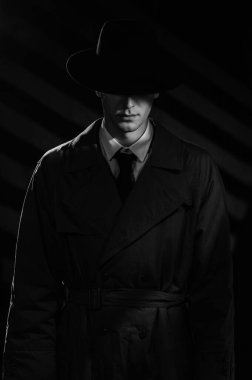 Siyah şapkalı ve ceketli bir erkek dedektifin koyu renk silueti. 1950 'lerin dedektif filmlerinin dramatik siyah portresi. Perdelerle ilgili dramatik bir ışık.