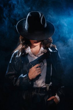 Silhouette: a female detective in a coat and hat with a gun in her hands. Dramatic noir portrait in the style of books and detective films of the 1950s