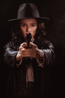 Silhouette of a female detective in a coat and hat with a gun in her hands pointing at the camera. A book drama noir portrait in the style of detectives of the 1950s